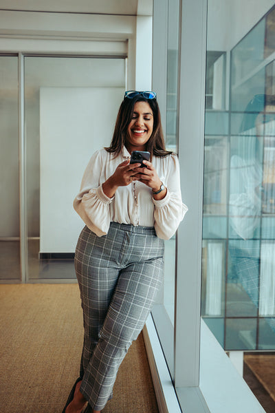 Successful Indian businesswoman at her office smiling while texting near office window