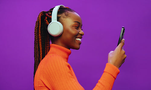 Happy woman listening to music on smartphone with vibrant purple background