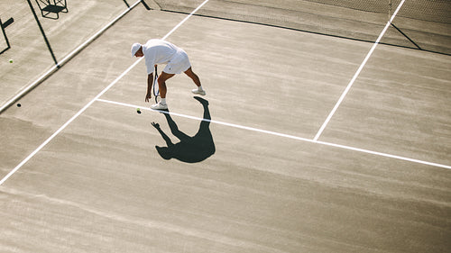 Senior man bending down to pick a tennis ball during a game of tennis