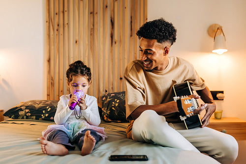 Cheerful single dad playing a guitar for his adorable daughter at home