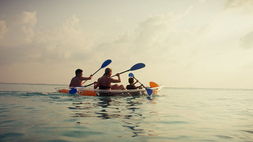 A family paddles kayaks across the calm tropical ocean under a bright, sunny sky