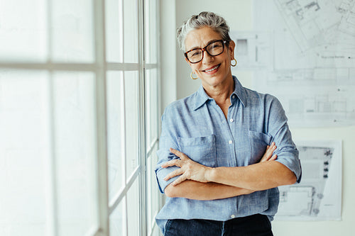 Happy female architect standing in her office with crossed arms