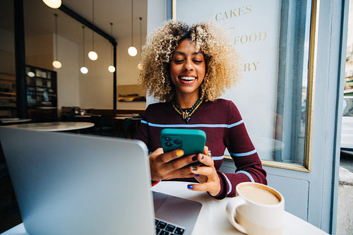 Young woman using smartphone and laptop in cafe