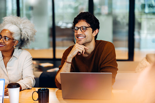 Smiling businessman with laptop in a busy office