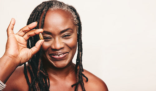Happy mature woman holding a capsule of Omega 3 fatty acids