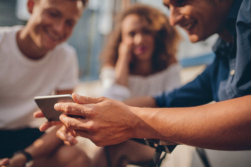 Young friends sitting outdoors and looking at smartphone
