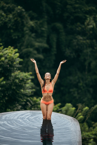 Young woman standing in pool with her arms raised
