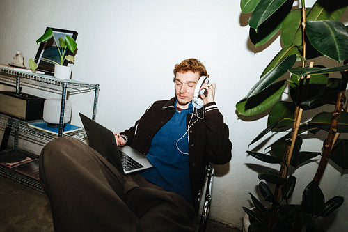 Young man multitasking with laptop and headphones in home office