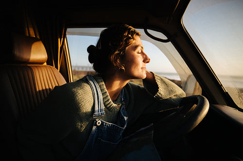 Peaceful woman rests her head on steering wheel during sunset