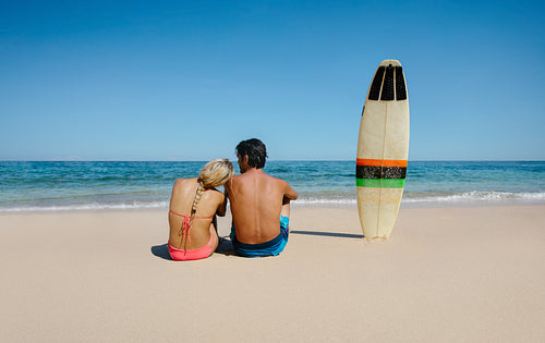 Couple relaxing on the sea shore with surfboard