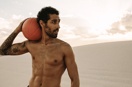 Muscular man with a exercise ball in desert