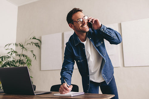Smiling businessman writing notes during a phone call