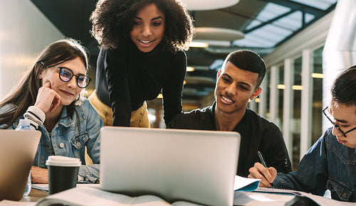 Four students using laptop for research at library