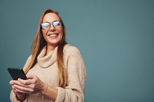 Happy blonde woman holding a smartphone in a studio