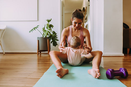 Cheerful mom working out with her baby at home