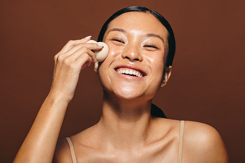 Applying face oil with a blender, woman massages her skin with a beauty sponge