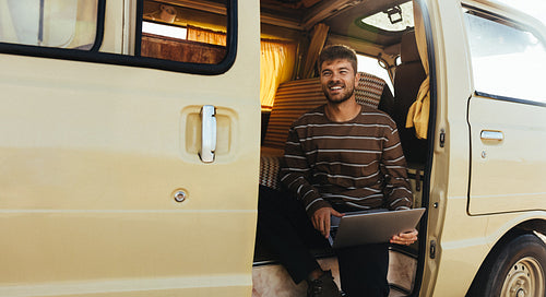 Fresh air break: Man sits at the van doorway with his laptop