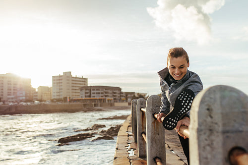 Smiling woman stretching on railing at seaside road