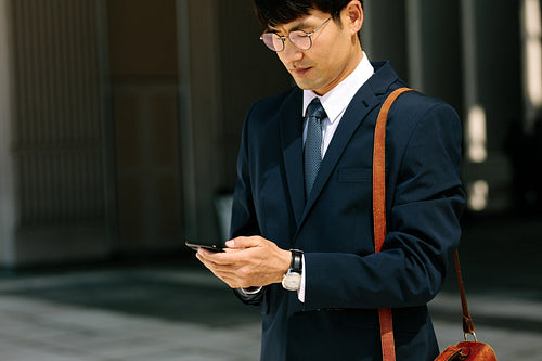 Asian businessman walking outdoors using smart phone
