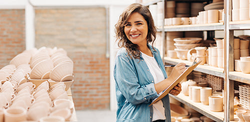 Happy young ceramist stocktaking in her shop