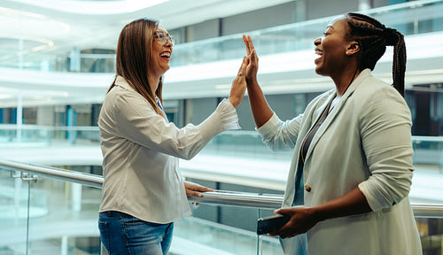 Two female colleagues sharing a high five in modern office