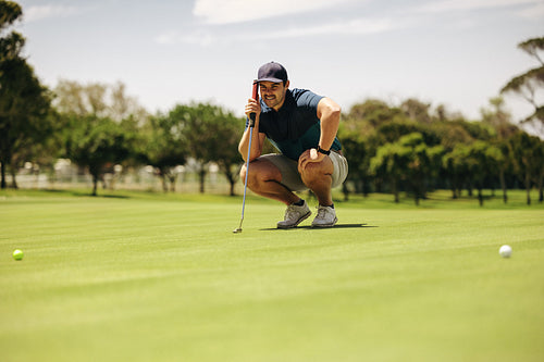 Caucasian man crouching and aiming on putting green, focusing on golf ball with a golf club in hand