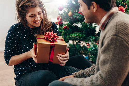 Young couple exchanging Christmas gifts at home.