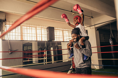 Happy boxer kid and coach celebrating victory standing inside boxing ring
