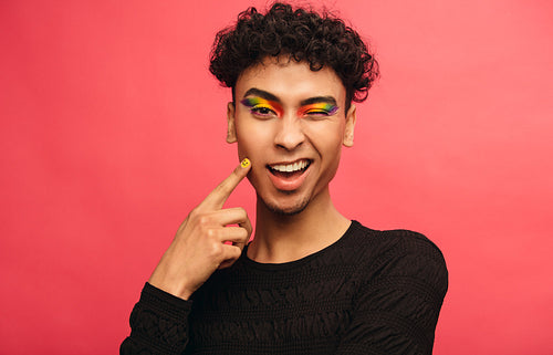Gay man with rainbow eyeshadow winking at camera
