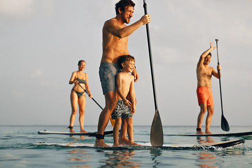 Father and son paddle boarding with family on a sunny summer day at sea