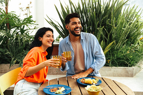 Latino friends enjoying an outdoor meal with drinks and laughter under the sun