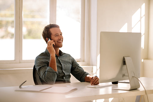 Entrepreneur talking on mobile phone while working on computer at home