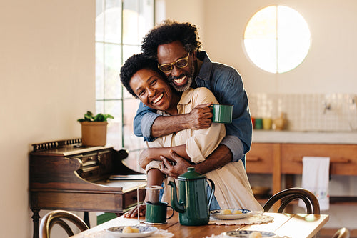 Romantic Afro-Brazilian husband hugging his wife at the breakfast table