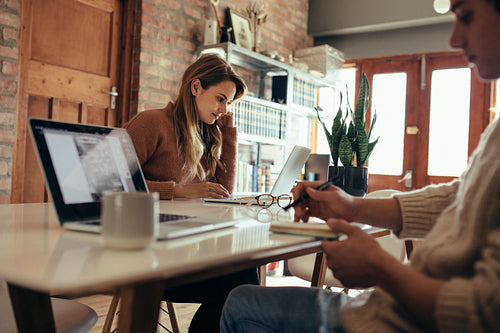 Woman sitting at table and working on laptop and her boyfriend