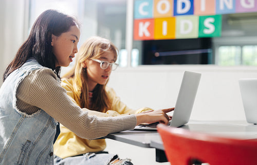 Computer-based learning for kids: Two girls assisting each other as they learn digital literacy and coding