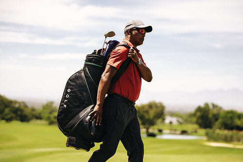Golf caddy walking on the fairway carrying a golf bag