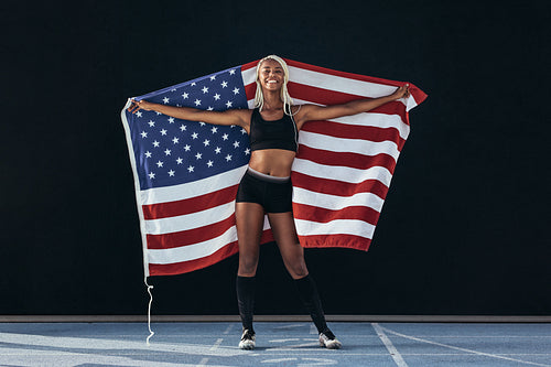 Female athlete standing on running track holding american flag