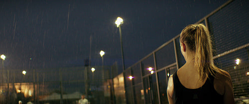 Female padel player serves during a competitive and intense match on a rainy night