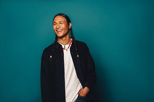 Ethnic man with braided hair and jewelry standing against a blue studio background