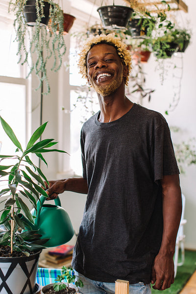 Smiling black man watering a flower pot at home
