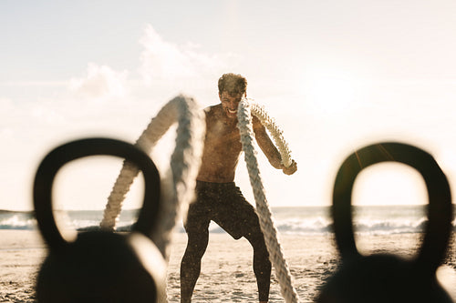Man doing fitness training at the beach with battle ropes and kettlebells