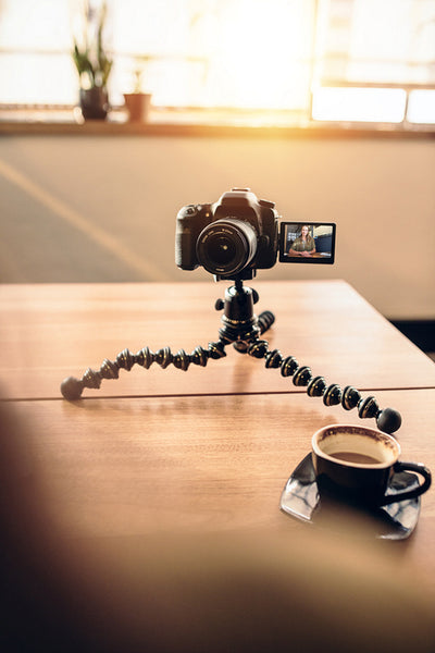 Desk of a photographer with coffee and tripod mounted digital camera.
