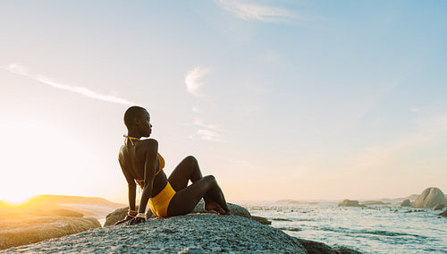African woman relaxing on a rock at the beach