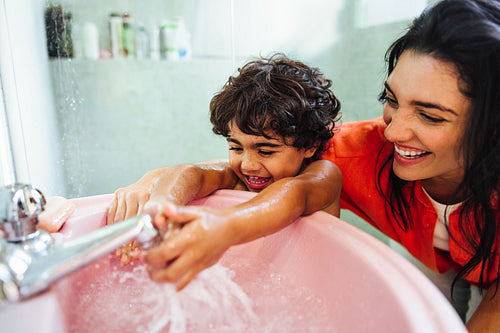 Mother joyfully engaging with her son while washing hands in a pink sink