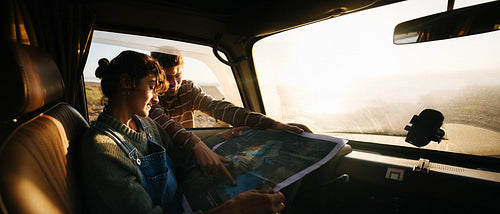 Couple on road trip studies a map inside a car at golden hour