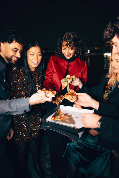 Friends sharing pizza outdoors during a festive evening celebration
