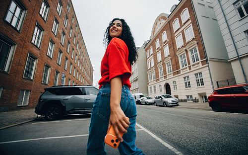 Woman walking to electric car charger with phone on urban street