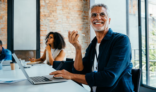 Joyful senior man in a modern office setting enjoying a productive meeting with diverse colleagues around a conference table