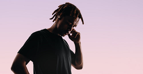 Tranquil young man standing in studio, enjoying music with wireless earbuds and closed eyes