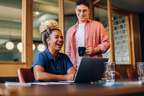 Smiling colleagues discussing work at a desk with a laptop and coffee